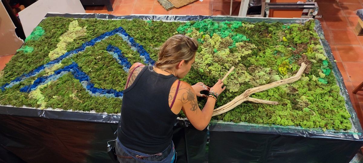 La artista montando un mapa vivo de musgo preservado con un río azul para una tienda