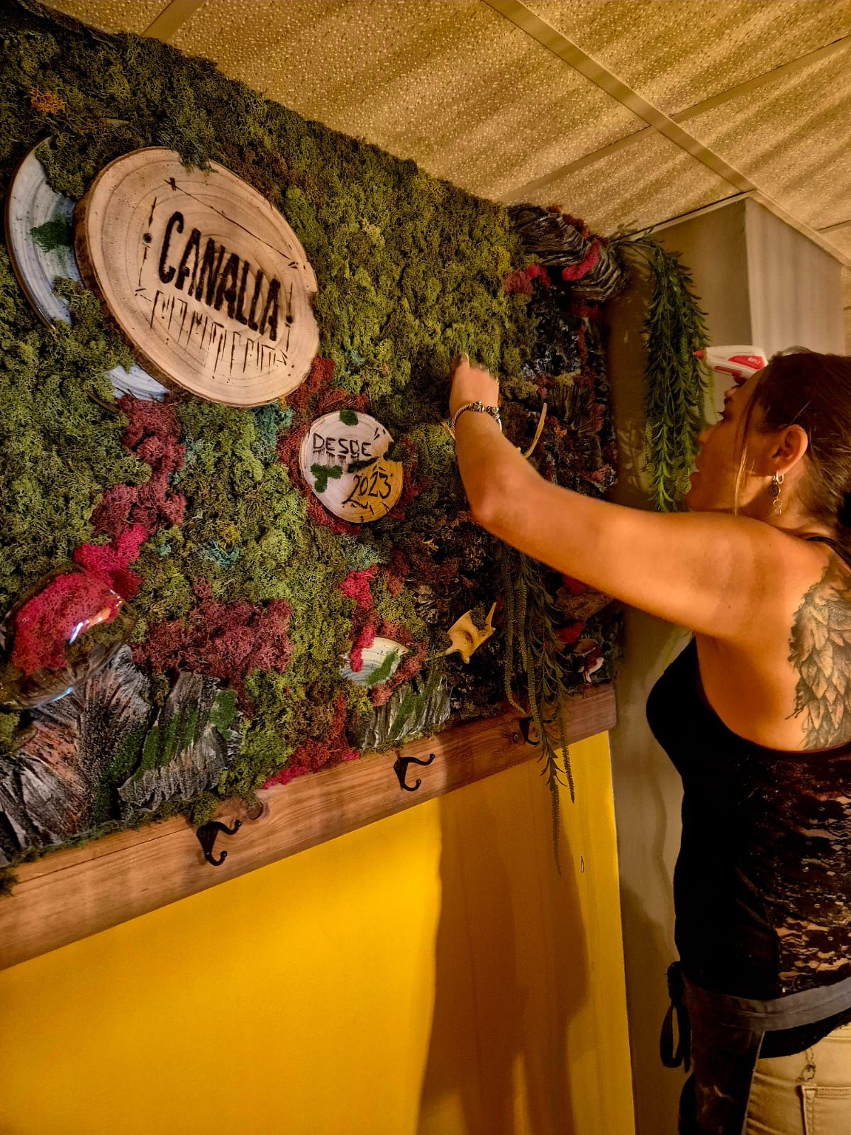 La artista instalando el jardín vertical de musgo preservado del restaurante Canalla