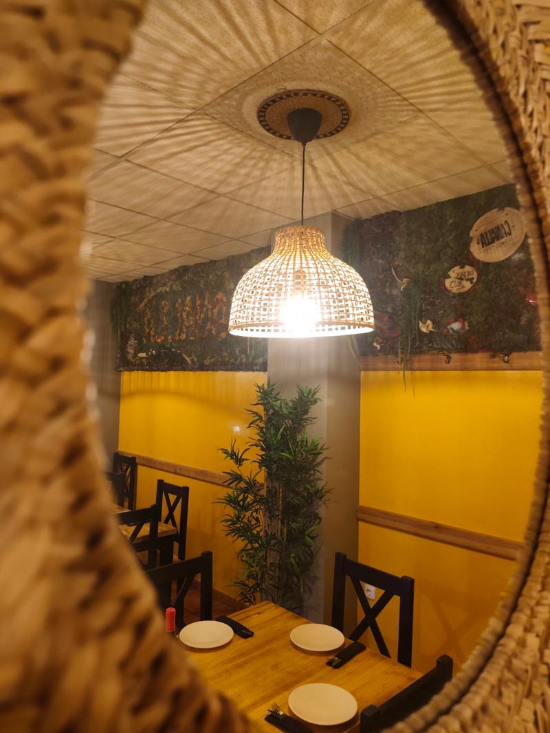 Comedor del restaurante con lámpara de mimbre y jardín vertical, visto a través de un espejo redondo